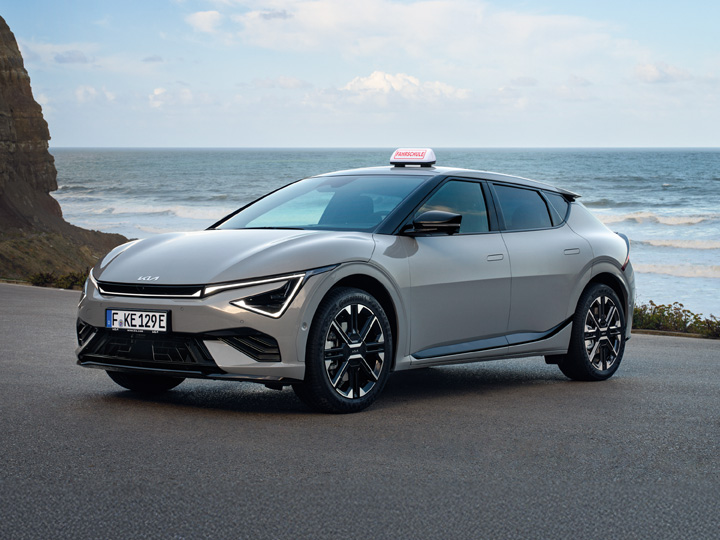 Der Kia EV6 aufgerüstet als Fahrschul-Fahrzeug auf einer Straße vor dem Meer.